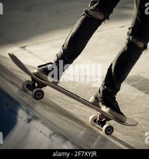 Nahaufnahme der Füße eines Teenagers auf einem Skateboard, das Tricks auf Halfpipe macht. Trendy junge Skater genießen im Freien auf dem Skatepark mit Skate Boa Stockfoto