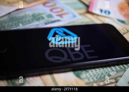 Viersen, Deutschland - 1. März. 2021: Nahaufnahme des Smartphones mit Logo-Schriftzug der australischen qbe-Versicherung auf Papiergeld-Währung Stockfoto