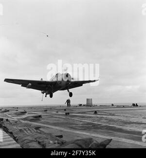 Der Grumman TBM-3S2 Avenger Submarine Boat Archter mit Registrierung 27 (1955-1961) des Marine Aviation Service (MLD) landet auf dem Flugzeugdeck des Flugzeuglagers hr.ms. Karel Doorman (R 81, ex-EHRWÜRDIGE Person), 1958. Der Bremshaken am Heck des Geräts ist herausgehoben und die Bremsseile am Flugdeck wurden leicht angezündet. Stockfoto