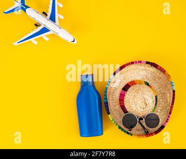 Flugzeug Sombrero Sonnenbrille und eine Tube Sonnencreme auf gelbem Hintergrund. Konzept für Sommerferien. Stockfoto