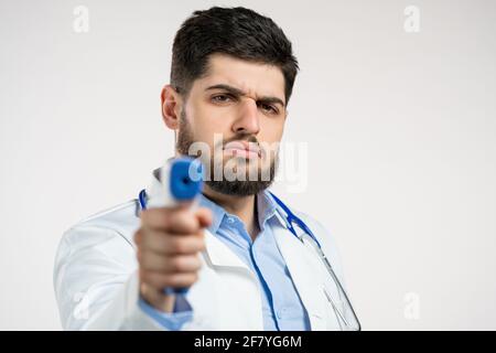 Der Arzt in weißem medizinischen Mantel leitet ein elektronisches berührungsloses Thermometer in die Kameralinse und misst die Temperatur. Stockfoto