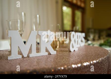 Nahaufnahme von Briefen mit der Aufschrift „MR & MRS“ auf einem Braune seidige Tischdecke mit leeren Champagnergläsern Stockfoto