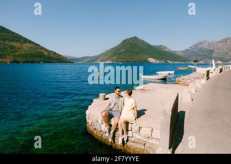 Ein Mann und eine Frau sitzen Seite an Seite Der Rand eines Piers in der Nähe von Perast in der Bucht Von Kotor Stockfoto