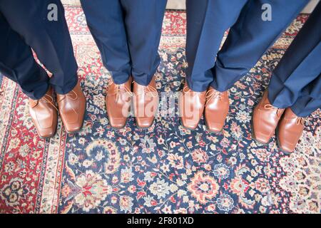 Aufnahme von vier Männerbeinen in einem hohen Winkel Blaue Hose und braune Lederschuhe Stockfoto