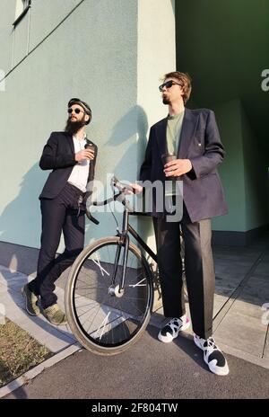 Zwei junge Freundinnen, die lässig angezogen waren, verbrachten Zeit zusammen in der Stadt und tranken beim nächsten Fahrrad Kaffee zum Mitnehmen. Stockfoto