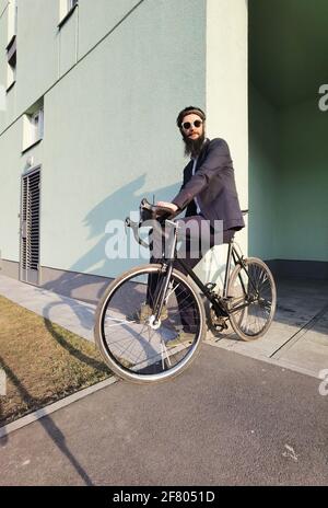 Starten Sie mit frischem Kaffee in den neuen Tag. Millennial Geschäftsmann hält eine Tasse Kaffee und lehnt sich an sein Fahrrad und schaut auf den freien Raum. Stockfoto