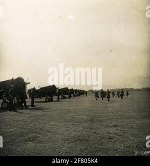 Ein Flughafen auf Java mit einer Reihe von Curtiss-Wright CW-21 Interceptor, der in einer Reihe von Abfangjägern der Militärluftfahrt der Royal Dutch Indian Army angeordnet ist. Eine Reihe von Drachen kommen um die Geräte herum. Stockfoto