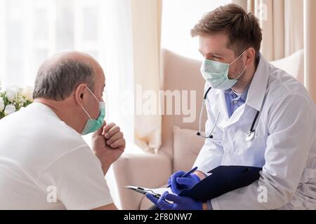 Arzt, der ein ärztliches Rezept an einen älteren Mann schreibt, der ihn besucht Zu Hause Stockfoto