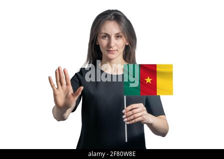 Glückliche junge weiße Frau, die Flagge von Kamerun hält und mit einem ernsten Gesicht ein Hand-Stopp-Schild auf weißem Hintergrund zeigt. Stockfoto