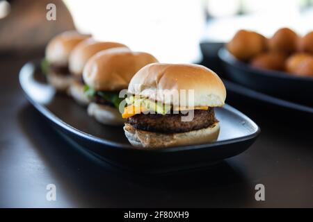 Mini-Hamburger werden auf einem langen schwarzen Teller serviert Stockfoto