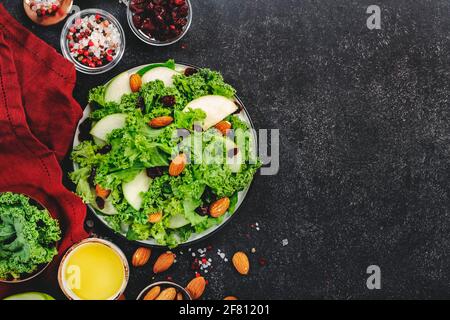 Kalesalat mit getrockneten Preiselbeeren, grünen Äpfeln und Mandeln. Vegan gesundes Essen, Draufsicht, schwarzer Küchentisch Stockfoto