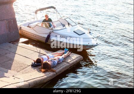 Sankt Petersburg, Russland - 27. August 2016: Zwei junge Mädchen ruhen auf einem Granitdamm neben einem festfahrenden Motorboot Stockfoto