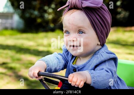 Nettes Baby Mädchen im Freien im Frühling halten Spielzeug Auto Rad Stockfoto