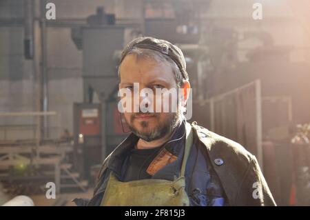 Ein Arbeiter mit einem Bart in Overalls in einem Produktionsraum in einer Fabrik. Nahaufnahme. Stockfoto