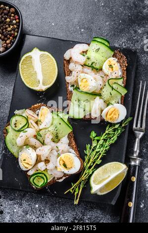 Frisches Toast mit Garnelen, Garnelen, Wachteleiern und Gurken auf Roggenbrot. Schwarzer Hintergrund. Draufsicht Stockfoto