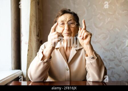 Eine sehr alte Frau zieht eine Brille an und schaut zu Die Kamera Stockfoto