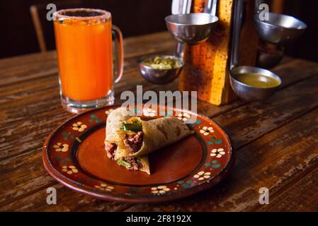 Burrito auf einem braunen Teller mit einem Orangensaft auf Ein Holztisch Stockfoto