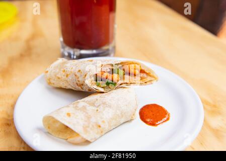 Vertikale Aufnahme von Burrito mit Clamato auf einem weißen Teller Und Bloody mary in einem durchsichtigen Glas Stockfoto