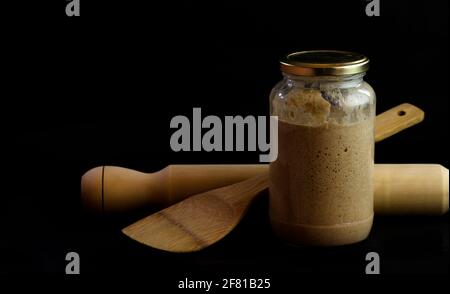 Nudelholz, Schöpfkelle und Teig im Glas bereit, um hausgemachtes Brot auf schwarzem Hintergrund zu machen Stockfoto