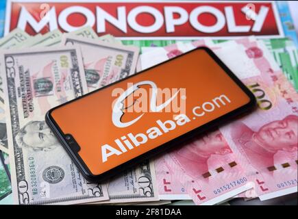 Alibaba-Logo auf dem Smartphone, das auf Geld platziert ist - US-Dollar und chinesischen Yuan, und Monopoly-Spiel auf dem verschwommenen Hintergrund. Konzept. Staffrod Stockfoto