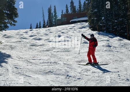 Skifahrer in leuchtend rotem Outfit, der während eines schönen sonnigen Wintertages auf der Piste posiert. Stockfoto