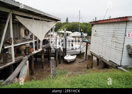 Yeppoon, Queensland, Australien - 2021. April: Bei Ebbe vertäuten Boote zwischen heruntergekommenen Hütten an einem alten Holzsteg im Küstenbach Stockfoto