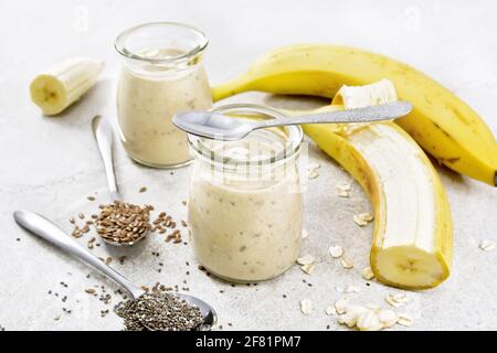 Milchshake mit Chiasamen, Leinsamen, Haferflocken, Puffreis und Banane in zwei Gläsern auf einem Tisch aus braunem Stein Stockfoto