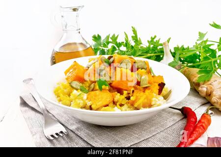 Hirsebrei mit würziger Kürbissauce und Samen auf einem Teller auf Serviette, Paprika, Ingwerwurzel, Knoblauch und Petersilie auf Holzbrett Hintergrund Stockfoto