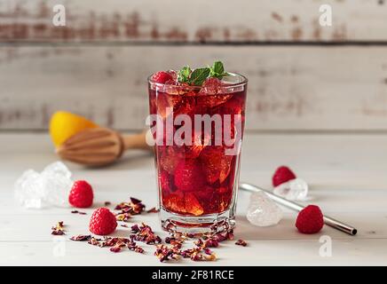 hibiskus-Eistee oder Karkade-Limonade mit Himbeeren, Minze und Zitrone auf einem Holztisch. Stockfoto