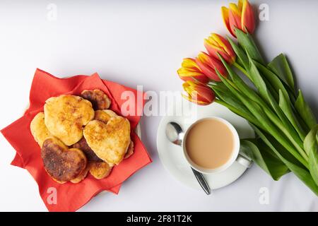 Eine Tasse Tee und auf einem Teller mit Servietten Syrniki in Form von Herzen steht Stockfoto