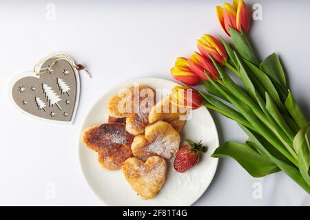 Ein weißer Teller neben einem Herzen und einem Strauß Von Tulpen mit Erdbeeren Stockfoto