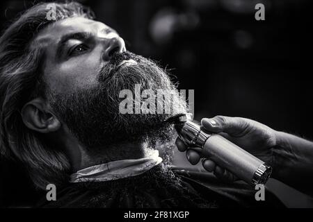 Bärtiger Mann im Friseurladen. Mann, der den Friseur im Friseursalon besucht. Der Friseur arbeitet mit einem Bartschneider. Hipster-Klient bekommt einen Haarschnitt. Hände Stockfoto