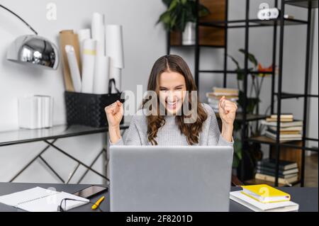 Verstanden. Aufgeregt junge Frau in Freizeitkleidung Schrei ja sitzen vor einem Laptop im modernen Büro, weibliche Mitarbeiter feiern besten Deal, Stellenangebot, gewinnen in Online-Lotterie, die Arme glücklich zu heben Stockfoto