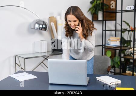 Eine vielbeschäftigte Frau, die am Telefon mit einem Kunden spricht und auf der Tastatur timt, in der Nähe des Büroschreibtisches steht und eine Büroangestellte multitasking-Frau beschäftigt Stockfoto