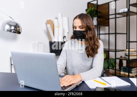 Weibliche Angestellte bleibt in Sicherheit vor Viruskrankheiten, die im Büro arbeiten, Frau trägt eine medizinische Maske und benutzt den Laptop in der Halle, um sich während einer Pandemie zu schützen Stockfoto