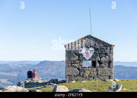 Ein Paar auf einem felsigen Hügel mit Blick auf eine schöne sitzen Landschaft neben einer alten Steinstruktur mit einem bemalten Herzen Stockfoto