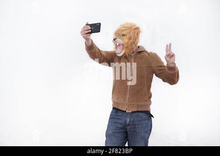 Ein Mann mit einem brüllenden Löwen voller Maske nimmt ein Selfie mit seinem Telefon isoliert auf weißem Hintergrund Stockfoto