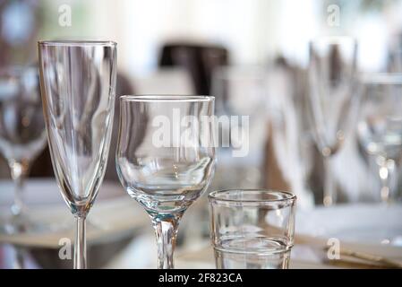 Im Restaurant wird ein Tisch mit Gläsern für Wein, Champagner und Cognac, Servietten und weißen Tellern für die Gäste serviert Stockfoto