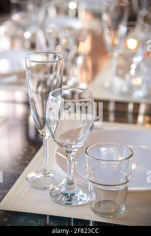 Im Restaurant wird ein Tisch mit Gläsern für Wein, Champagner und Cognac, Servietten und weißen Tellern für die Gäste serviert Stockfoto