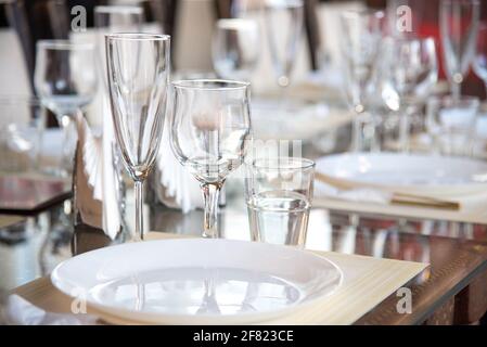 Im Restaurant wird ein Tisch mit Gläsern für Wein, Champagner und Cognac, Servietten und weißen Tellern für die Gäste serviert Stockfoto