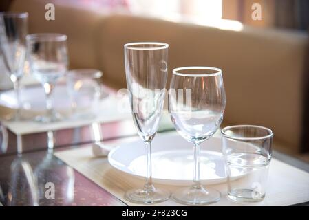 Im Restaurant wird ein Tisch mit Gläsern für Wein, Champagner und Cognac, Servietten und weißen Tellern für die Gäste serviert Stockfoto