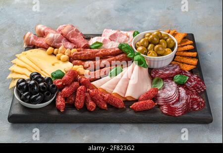 Vorspeisen-Bretter, Fleisch- und Käseschneiden mit Basilikum und Oliven auf einem rechteckigen Brett auf grauem Hintergrund. Seitenansicht. Stockfoto