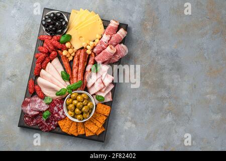 Vorspeise mit Fleisch und Käse, Oliven und Basilikum auf grauem Hintergrund. Draufsicht mit Kopierbereich. Stockfoto