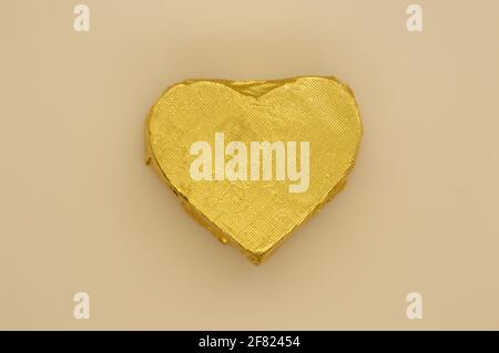 Bonbon-Verpackung aus Gold in Herzform auf hellbeigem Hintergrund. Stockfoto