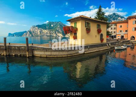 Festgetäute Holzboote und ein farbenfrohes, niedliches Gebäude mit Blumen am Pier. Kleiner Hafen und spektakuläre Uferpromenade in Torbole, Gardasee, Ita Stockfoto