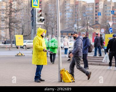 Moskau. Russland. März 26, 2021. Ein Mann in einem gelben Regenmantel und einer medizinischen Maske verteilt politische Propagandazeitungen an die Passanten Stockfoto