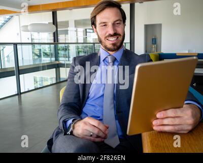 Entspannter Geschäftsmann mit seinem PC-Tablet, während er im Büro sitzt Stockfoto