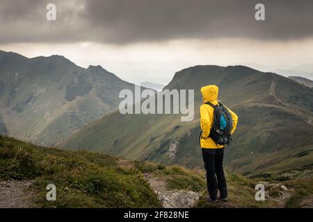 Wanderer mit Blick auf den wolkigen Himmel über den Bergen. Frau, die bei schlechtem Wetter in den Bergen wandert. Abenteuer in der Natur Stockfoto