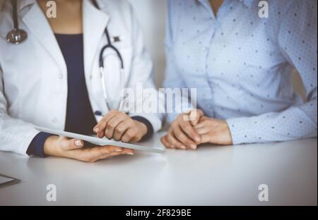 Unbekannte Ärztin zeigt ihrem Patienten eine Beschreibung der Medikation, während sie zusammen am Schreibtisch im Schrank in einer Klinik sitzt. Weiblich Stockfoto