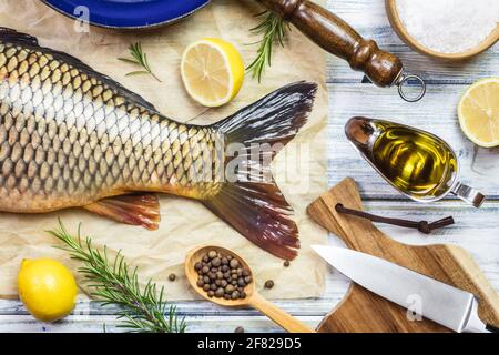 Fisch zum Kochen. Karpfen und Zutaten auf weißem Tisch. Gesunde Lebensmittel zubereiten. Flach liegend Stockfoto